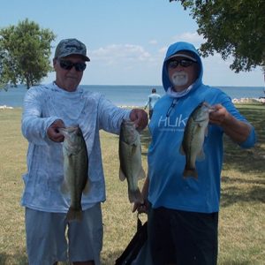 2 men in hoodie tees hold up 3 bass in front of Lake Tawakoni