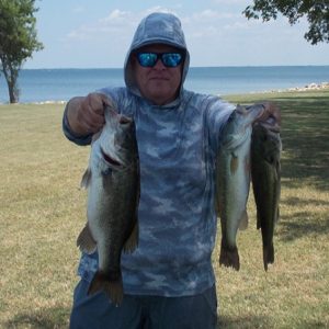 person in camo hoodie hold 3 bass in front of Lake Tawakoni