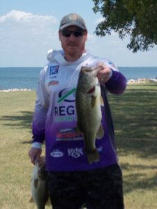 tall man in hoodie and cap holding large bass in front of Lake Tawakoni