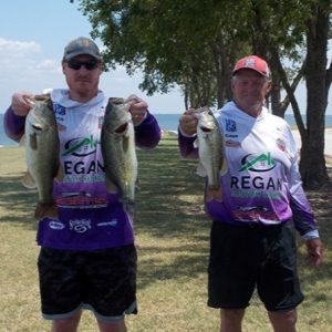 2 men in caps and hoodies holding 3 bass in front of Lake Tawakoni