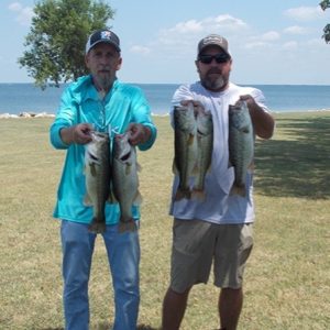 2 men in caps hold 4 bass in front of Lake Tawakoni