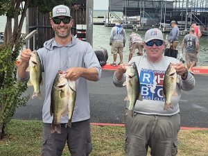 tall man in grey cap and shirt holds 2 fish next to man in RHBC shirt and cap holding 2 fish