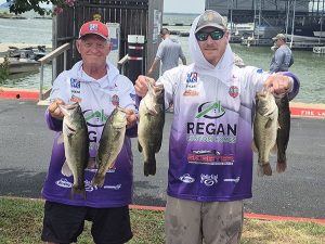 2 men in purple and white Regan hoodies show off 2 bass fish each at lake