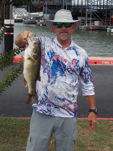 man in wide brimmed hat and blue/pink patterned shirt holds up 1 fish