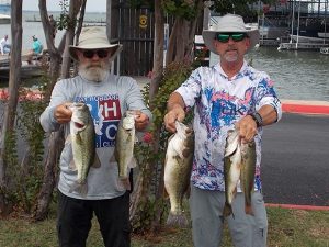 2 men pose holding 2 fish each; man on left with tan hat and RHBC shirt and long beard, man on right in blue and pink floral shirt, wide brimmed hat and sunglasses
