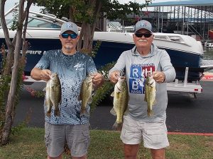 2 men pose with bass fish in front of boat at lake marina