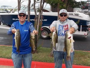 2 men holding 2 fish each in front of boats at lake marina