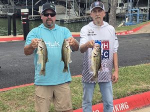 man in teal blue shirt holds 2 fish, man in white shirt holds 1 fish