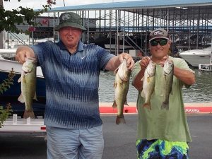 2 men pose holding 2 fish each in front of lake