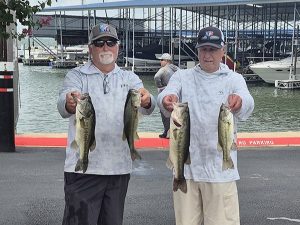 2 men holding 2 fish each in front of lake