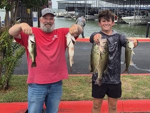 2 men holding 2 fish; man on left in red shirt with beard, man on right in dark shirt and hat