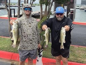 man in camo hoodie and cap holds 2 fish, man in black shirt holds 2 fish